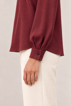 Blusa satinada con cuello alto y pliegues en burdeos, detalle del puño