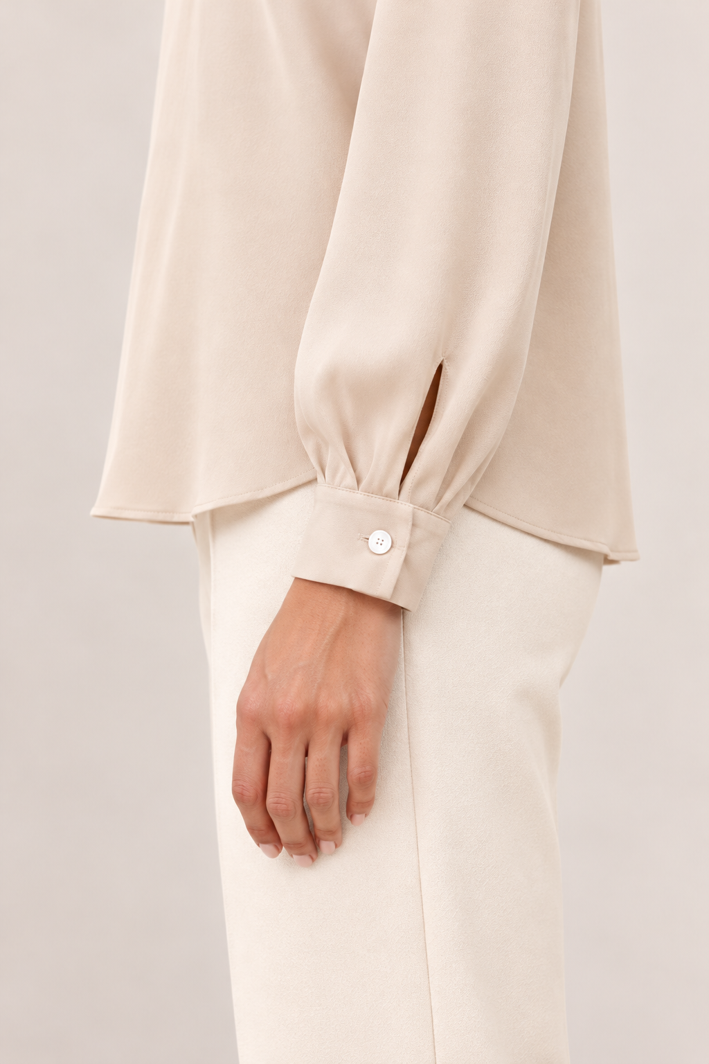 Blusa satinada con cuello alto y pliegues en marfil, detalle del puño
